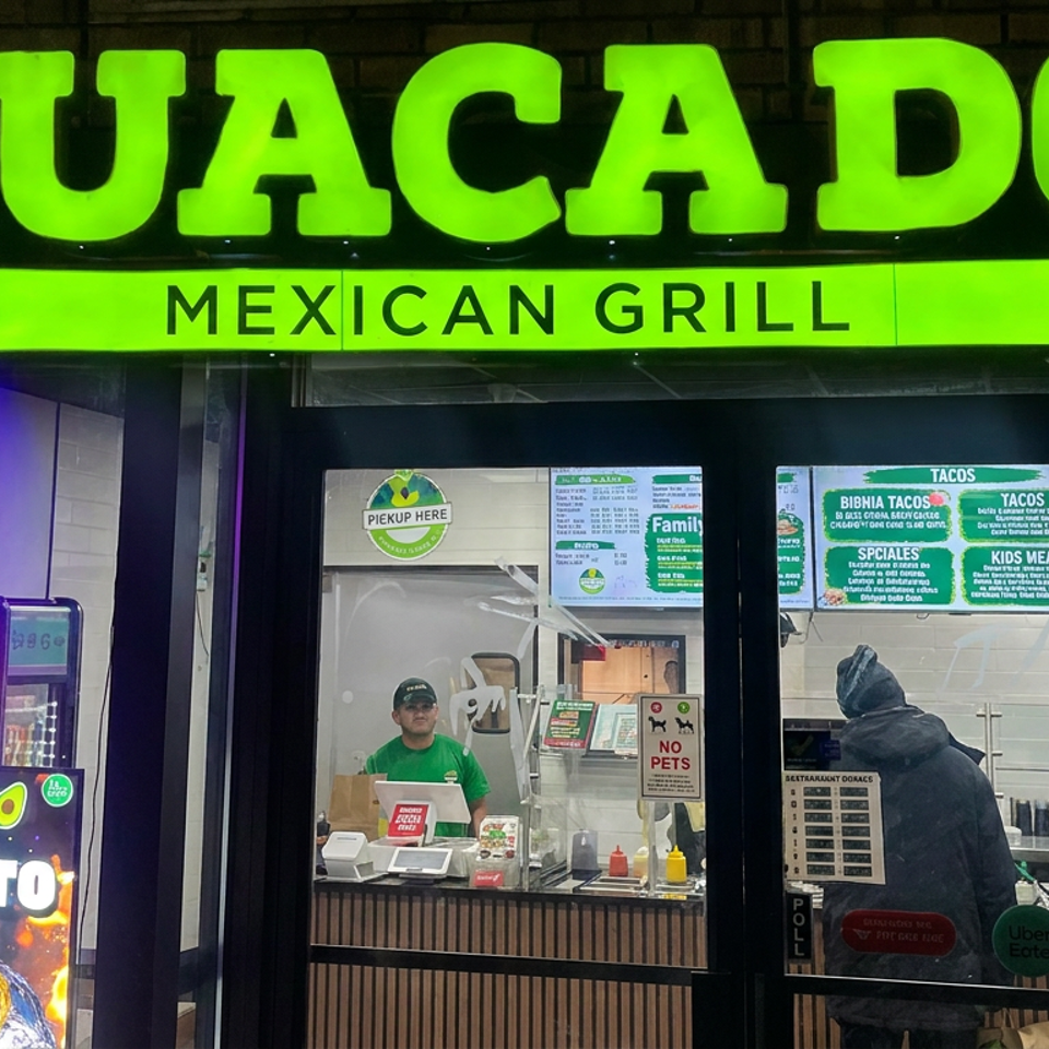 Guacadoo Mexican Grill storefront with bright green signage, neon open sign, burrito poster, employee, and customer at the counter.
